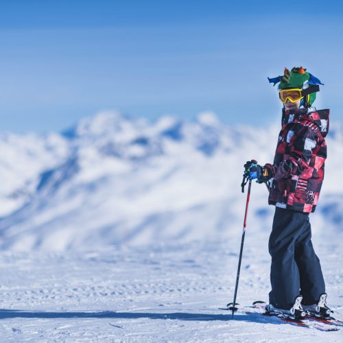 Young male skier in colorful outfit on top of mountain ski resort. Copy space for text.